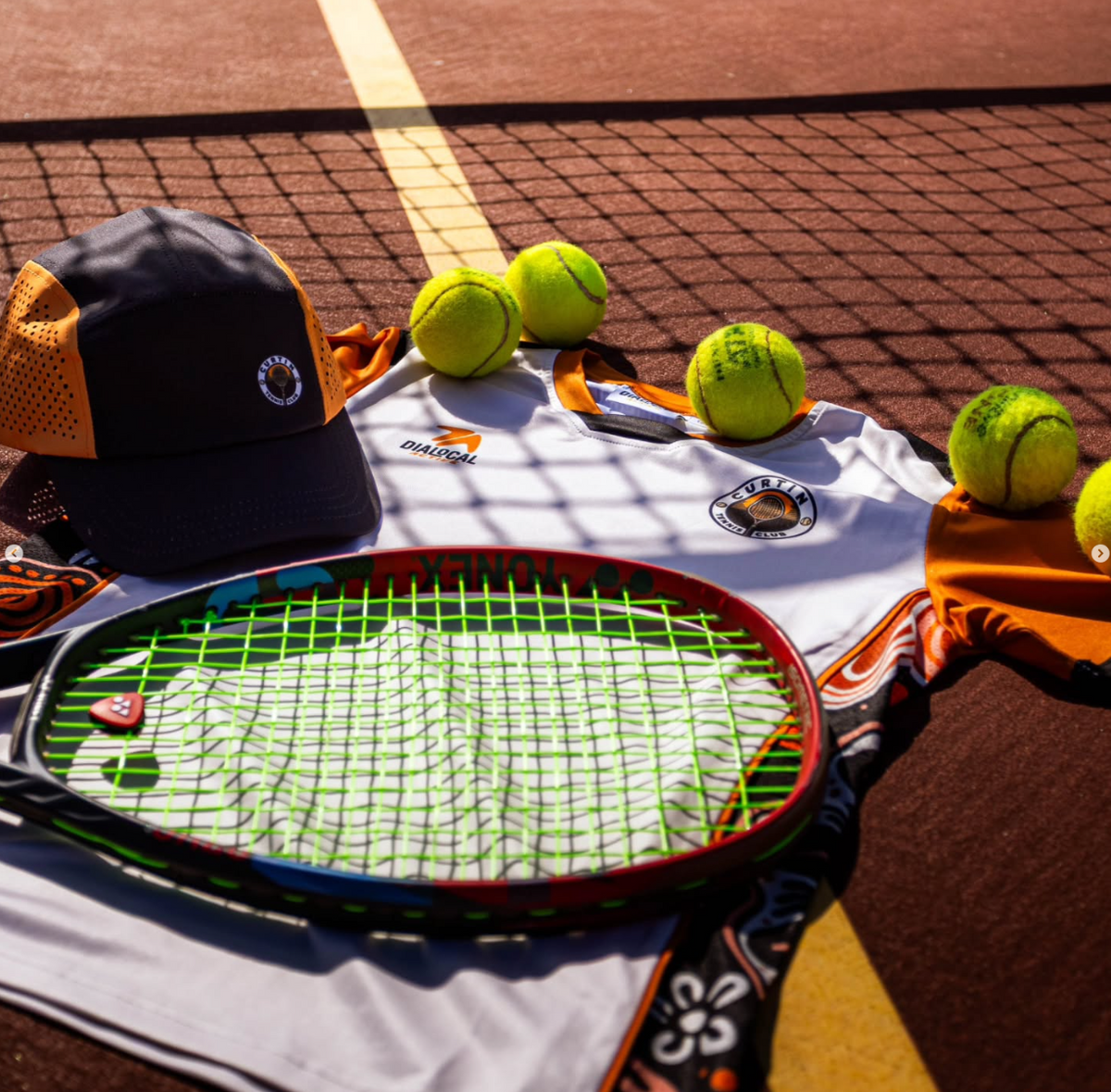Curtin tennis shirt, racquet and tennis balls on court