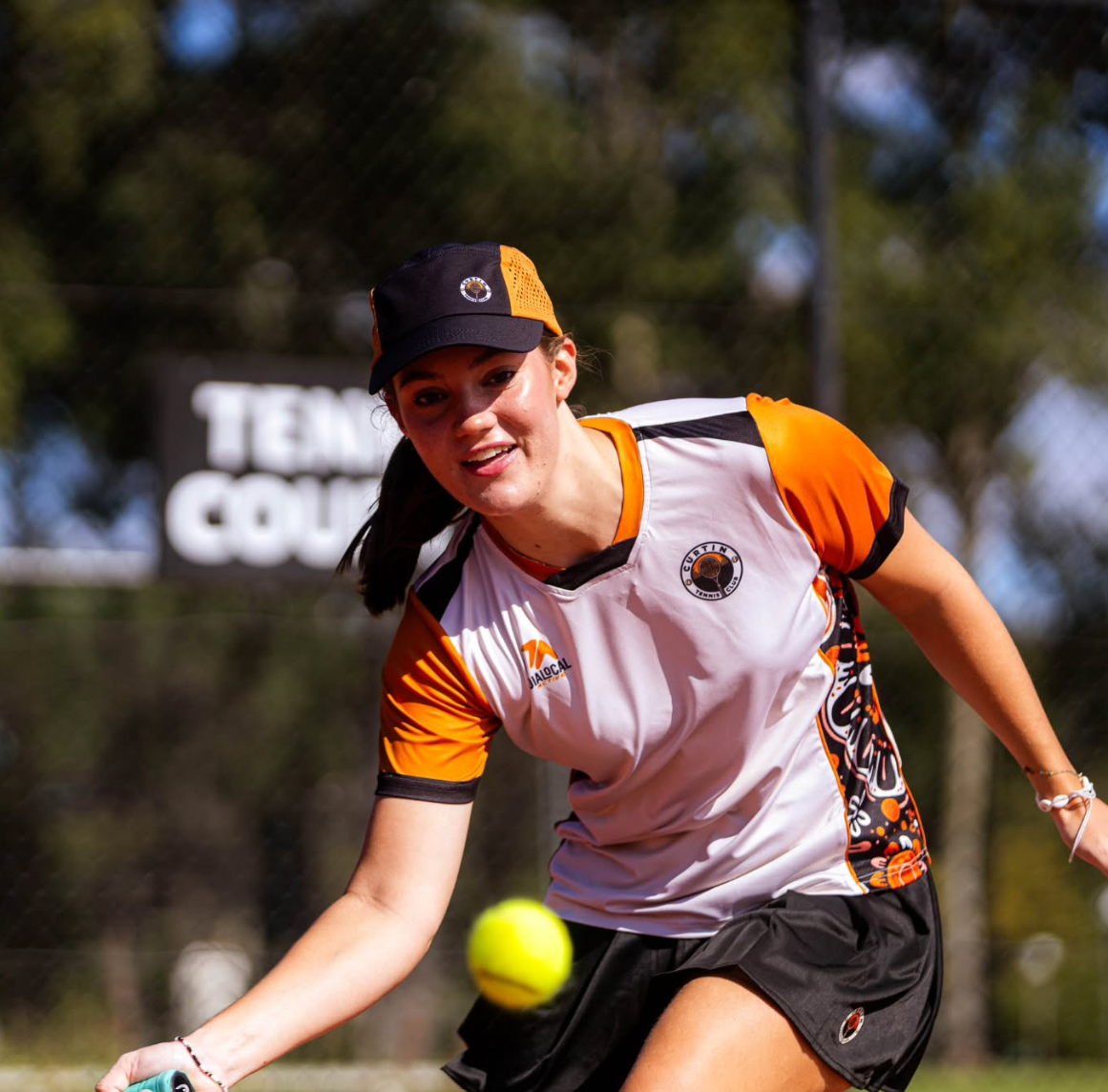 Curtin tennis player reaching for a ball in the club kit